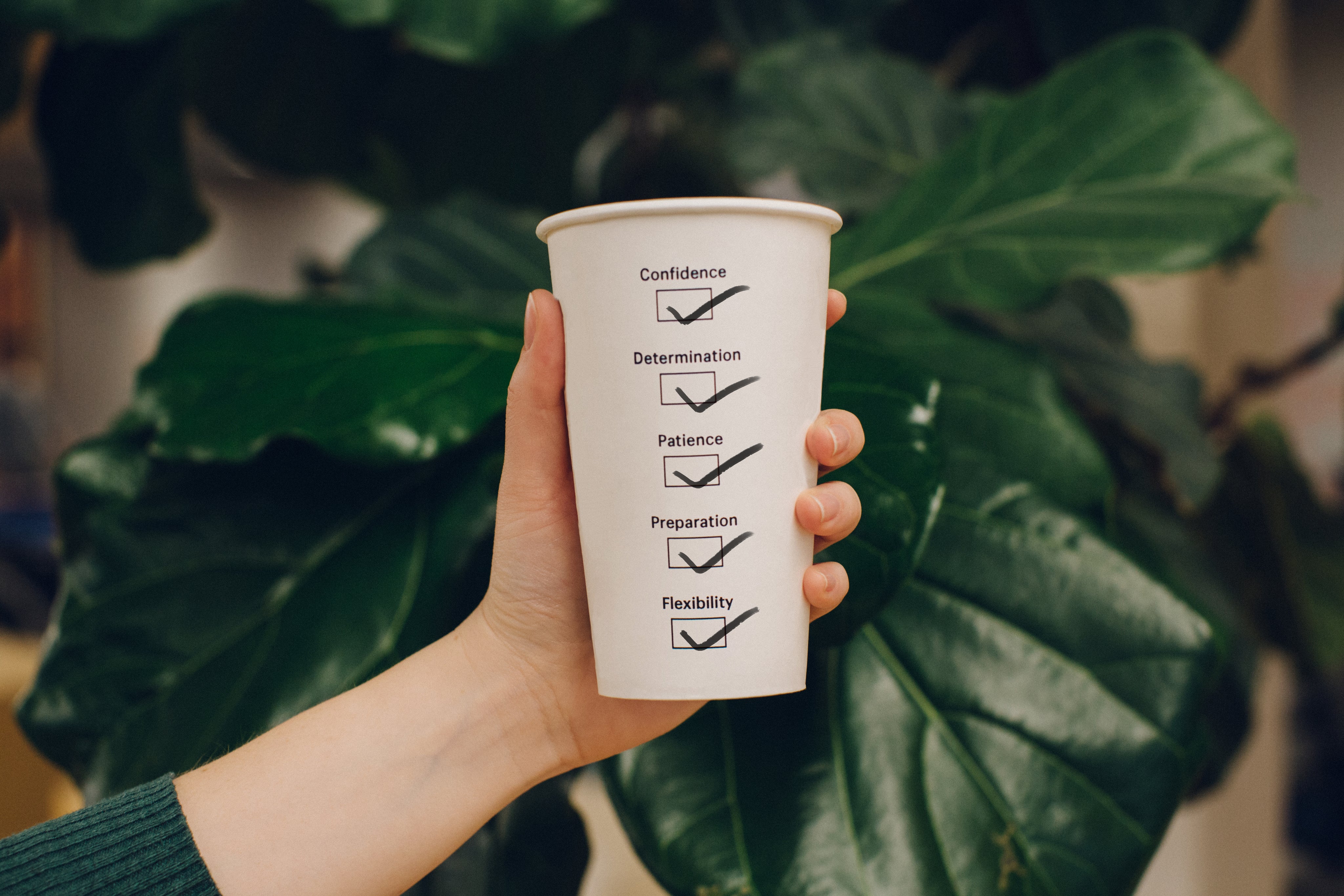 Hand holding a disposable coffee cup with a motivational checklist printed on side of cup