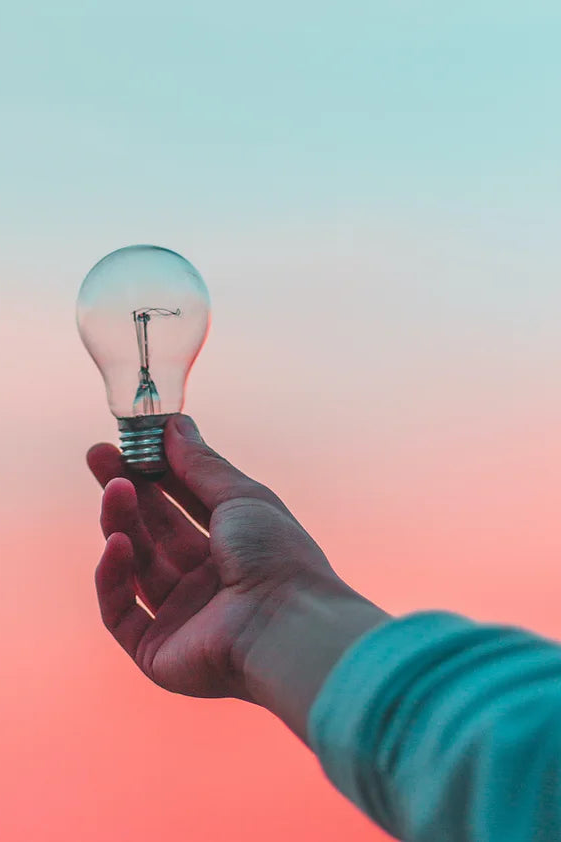 Hand holding a light bulb with sunset